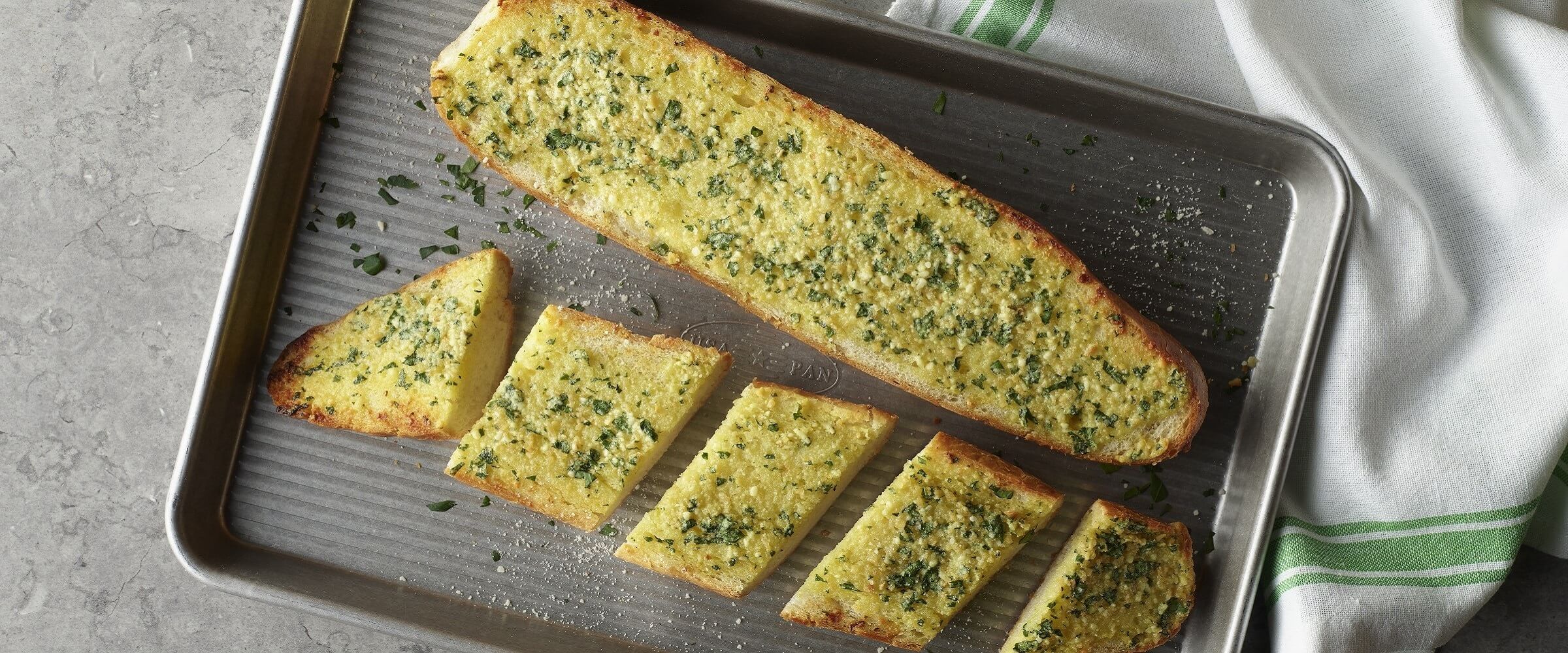 Garlic bread with seasoning on sheet pan next to linen napkin