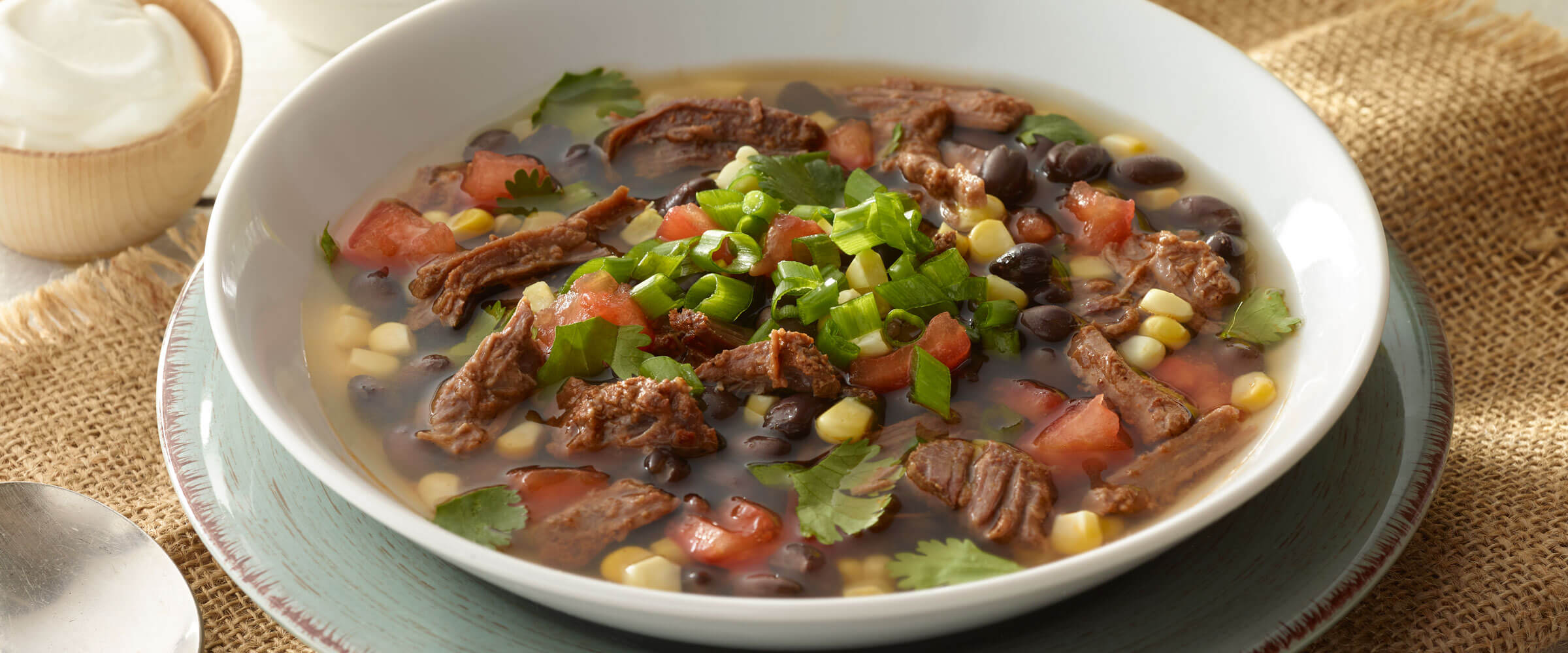 Hearty Beef & Black Bean soup topped with green onions in a white bowl