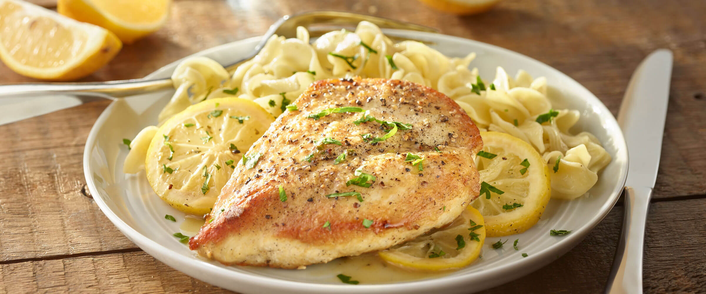 Lemon Garlic Chicken on plate with utensils and lemon wedges