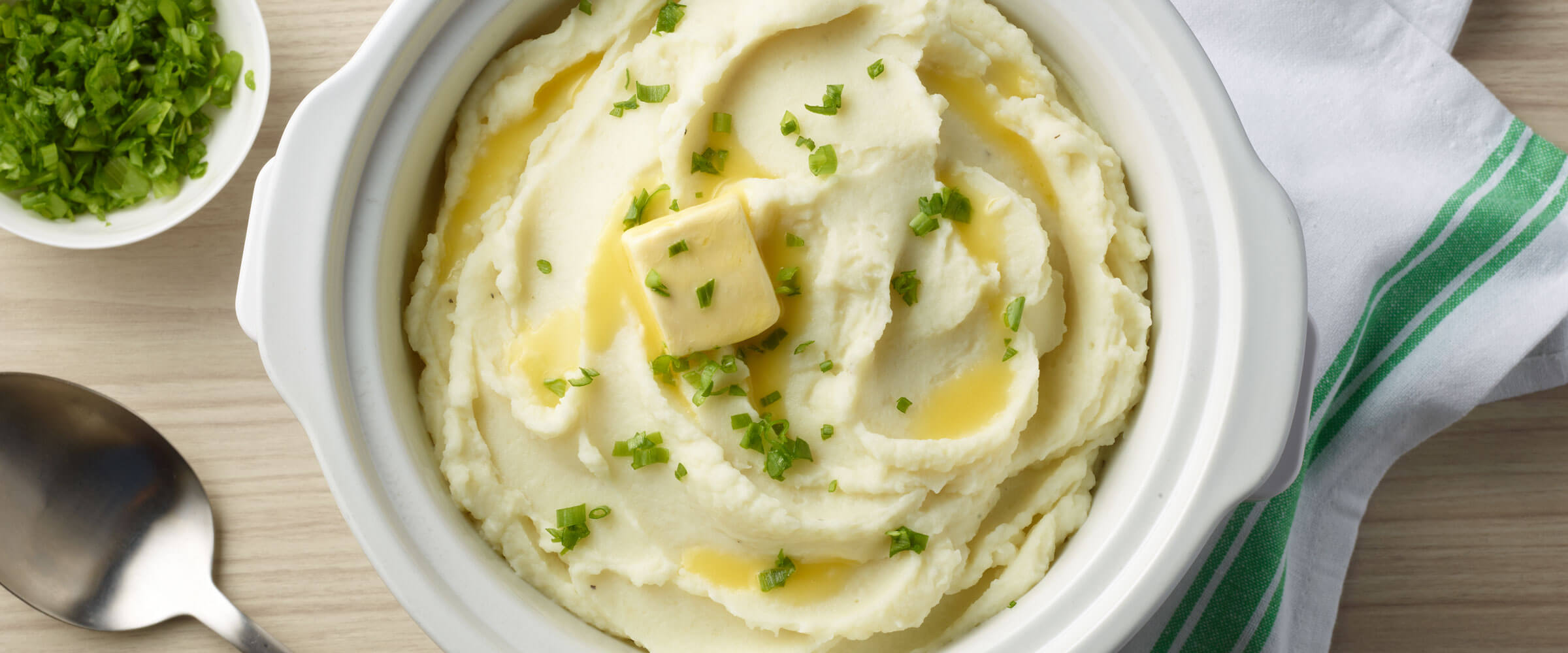 Slow-Cooker Mashed Potatoes topped with butter and garnish in white dish
