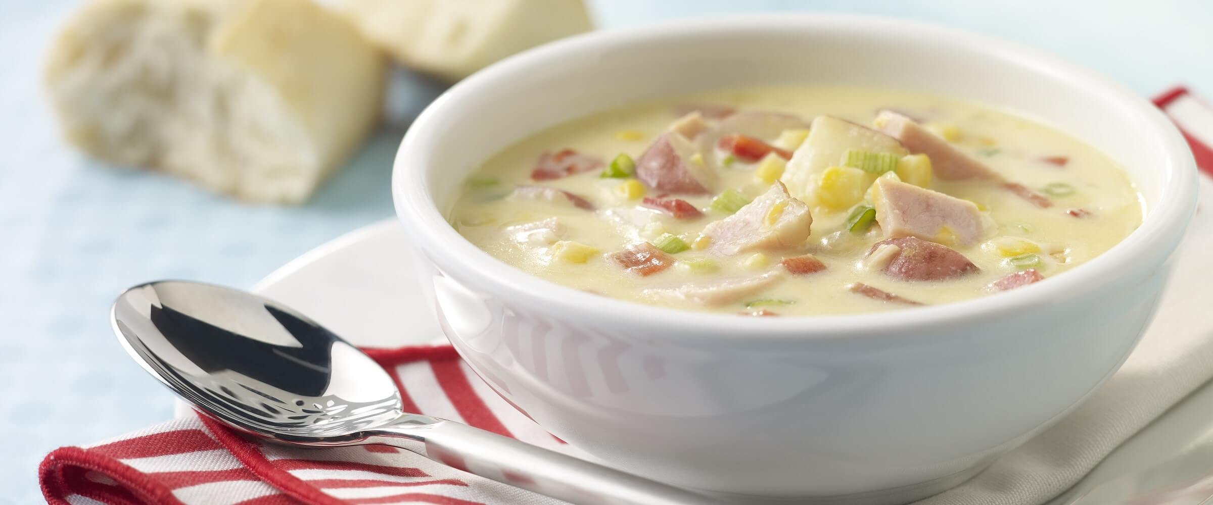 Cheesy ham and corn chowder in white bowl with spoon and red and white napkin