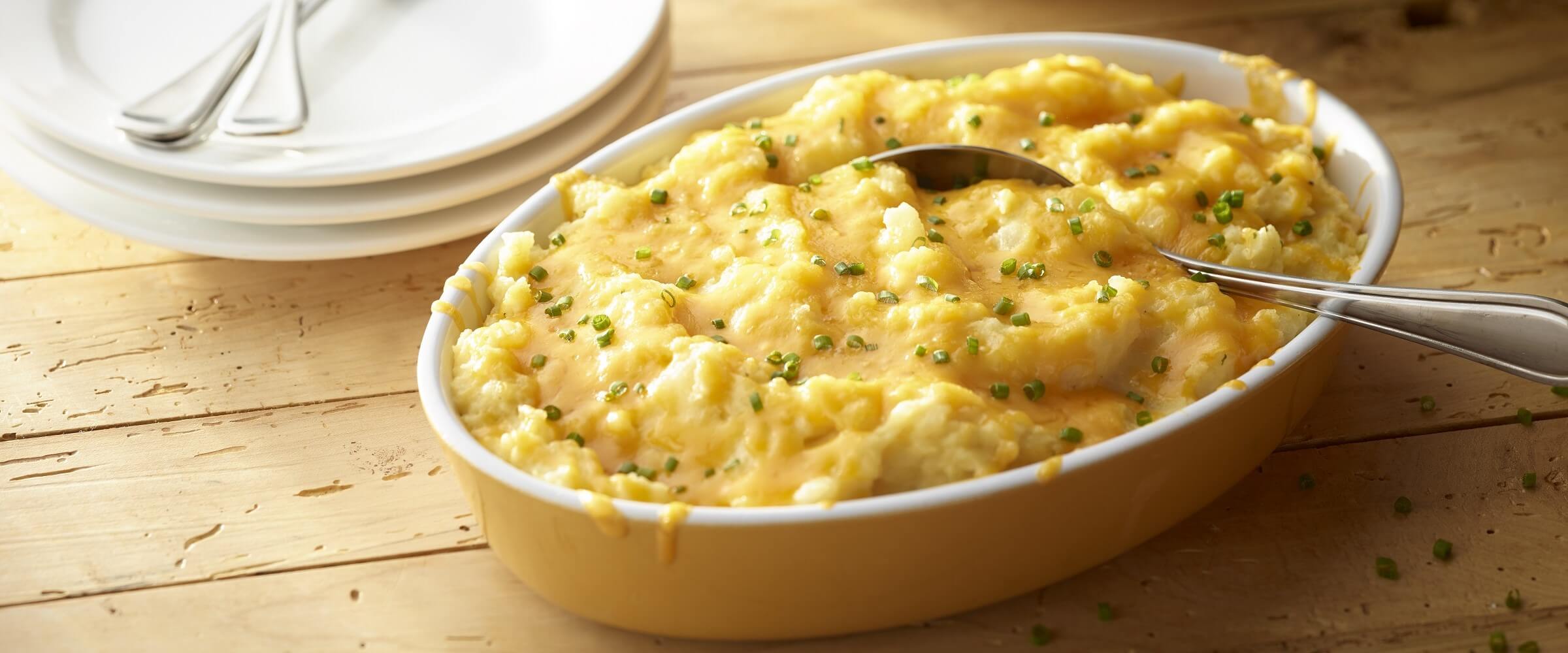 Cheesy mashed potatoes in yellow bowl with garnish and a spoon