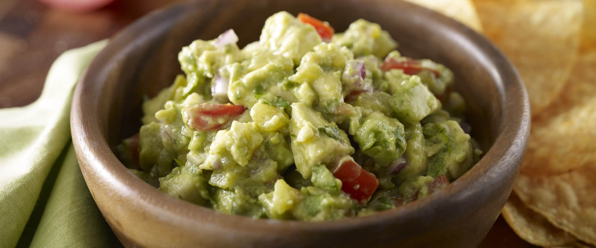 Garden guacamole in brown bowl with chips on side