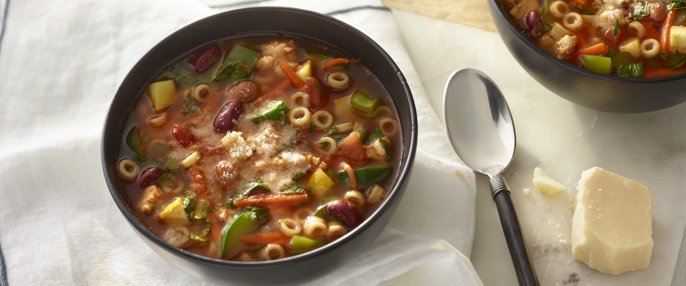 Italian minestrone soup in black bowl with spoon and parmesan cheese