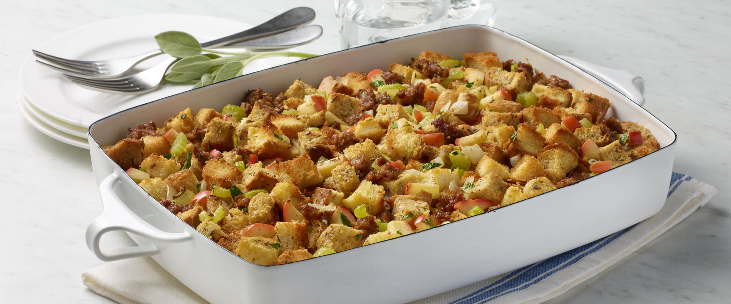 Sausage and Herb Stuffing in white dish with serving plates on the side
