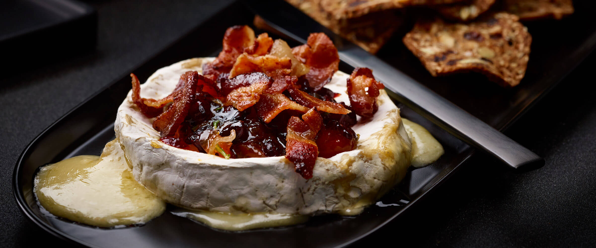 Bacon Cranberry Baked Brie on black platter with knife