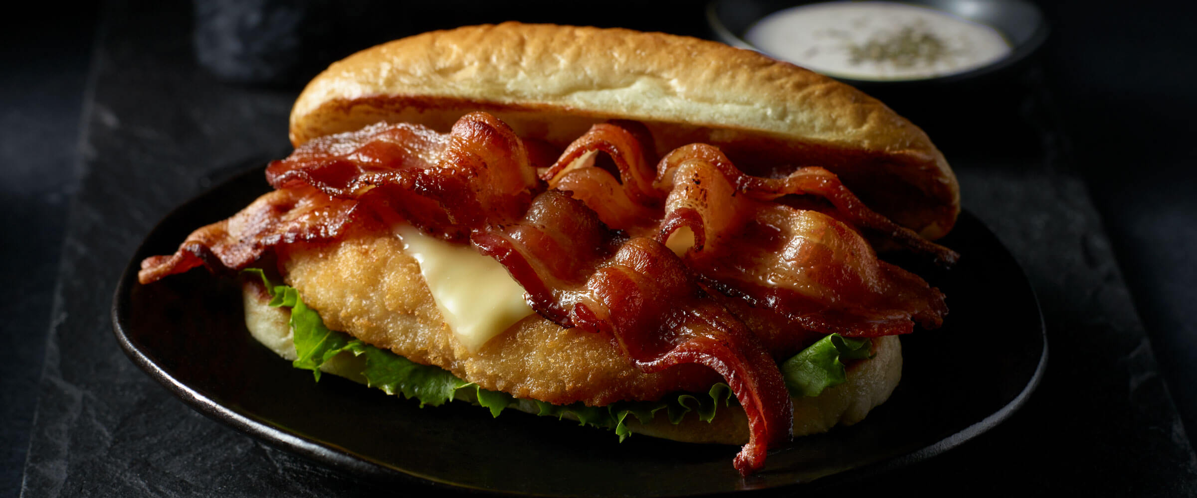 Bacon Chicken Sandwich on black plate with dipping sauce