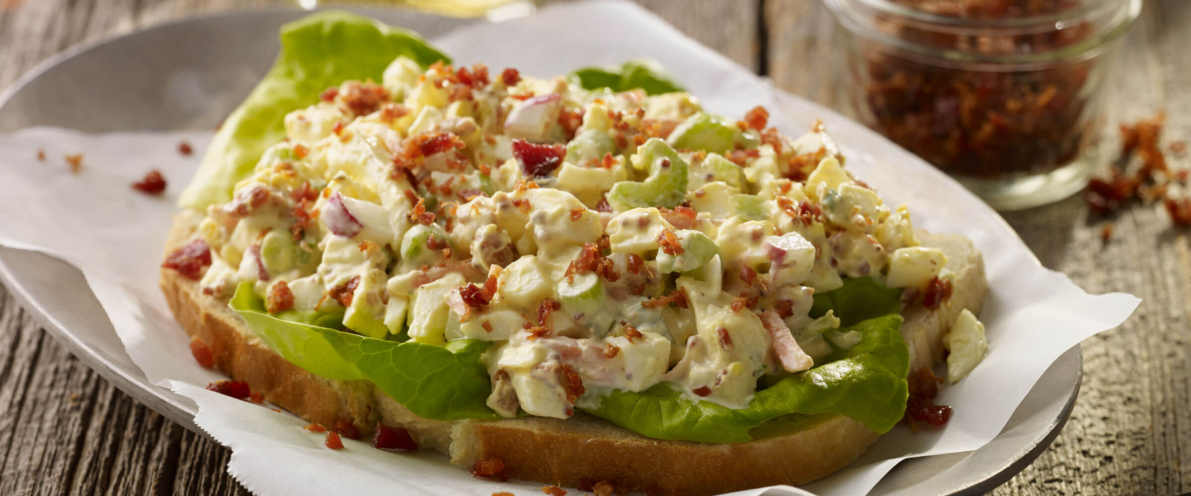 Garden egg salad with bacon on slice of bread on parchment paper