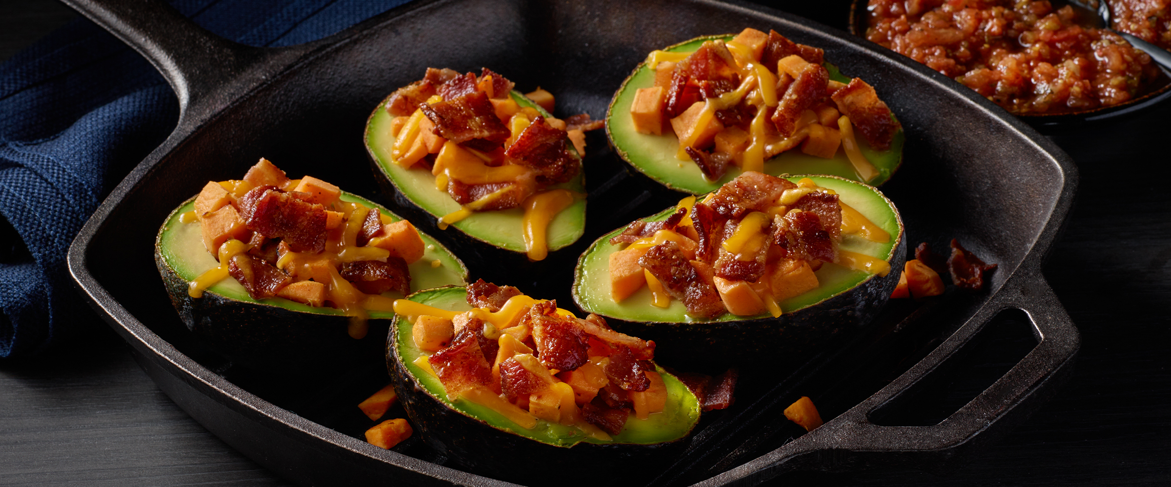 Five bacon, sweet potato, avocado breakfast stuffers in a cast iron skillet.