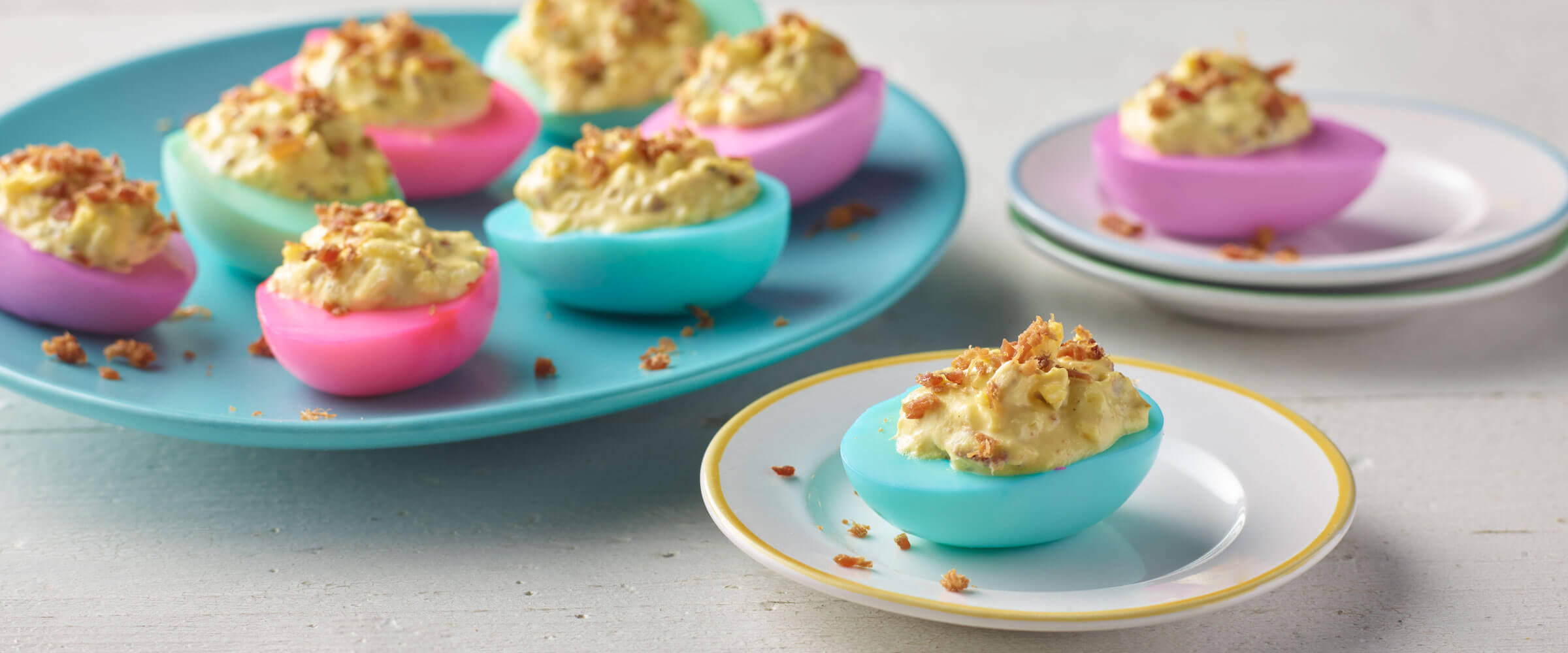 Spring Deviled Eggs dyed pink, blue and purple topped with bacon bits
