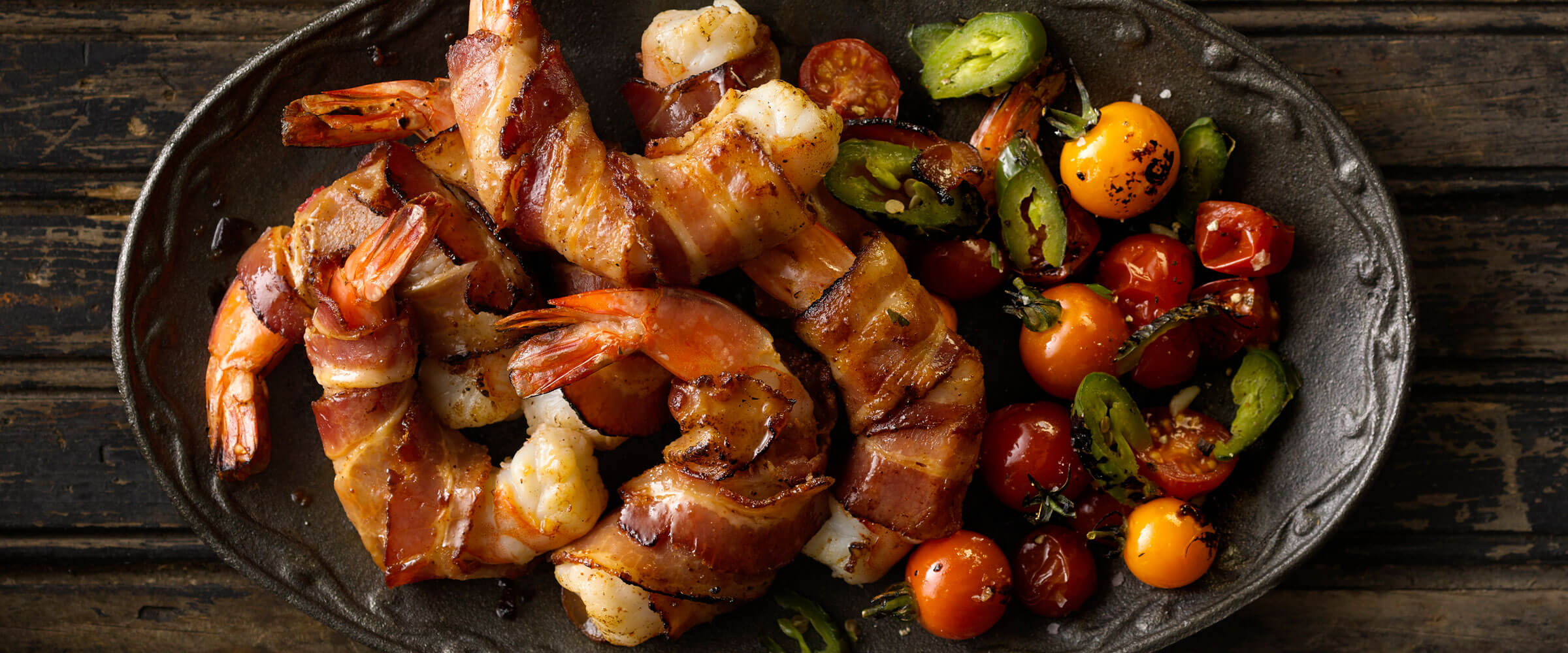 Jalapeno bacon wrapped shrimp with roasted tomatoes and peppers on black plate
