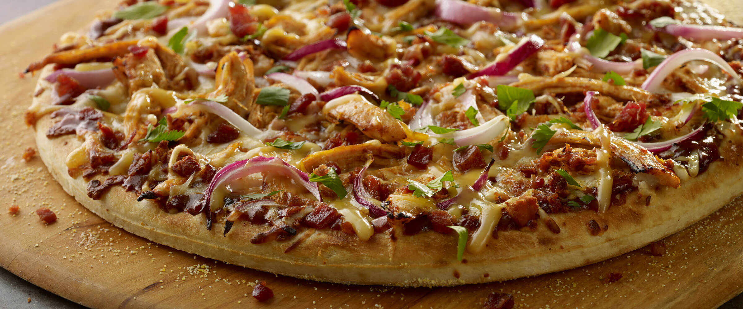 BBQ Chicken Bacon Pizza topped with red onions on pizza board