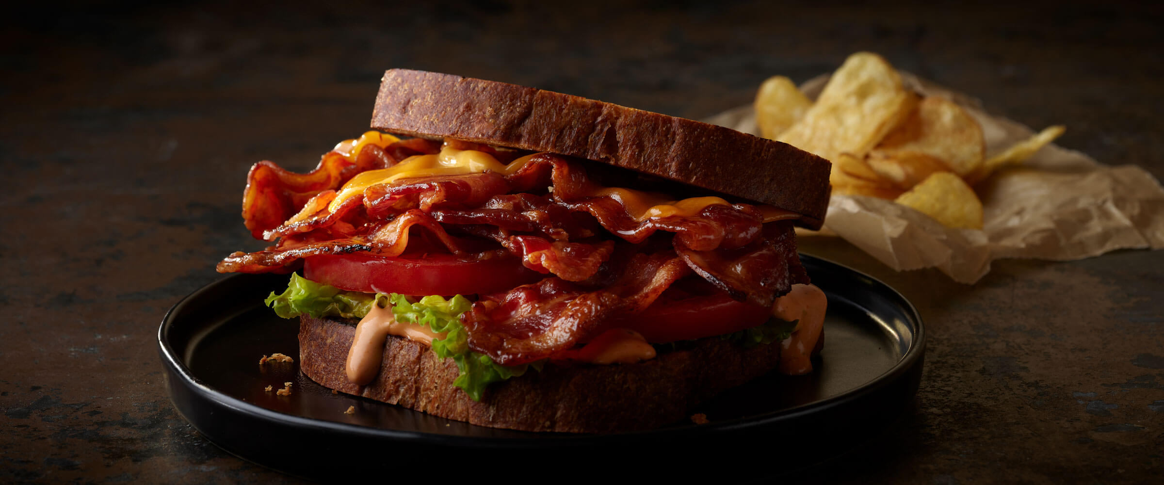 BLT with Cheese on black plate with side of chips