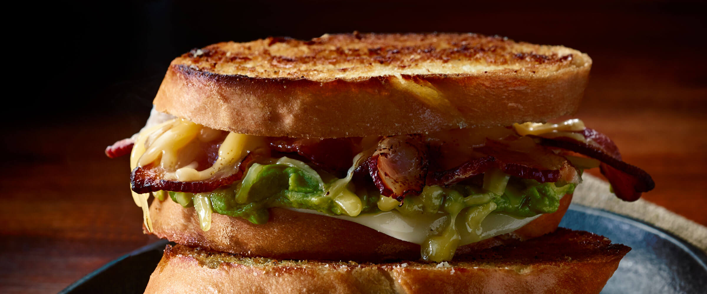 Grilled Cheese, Bacon and Guacamole Sandwich on black plate