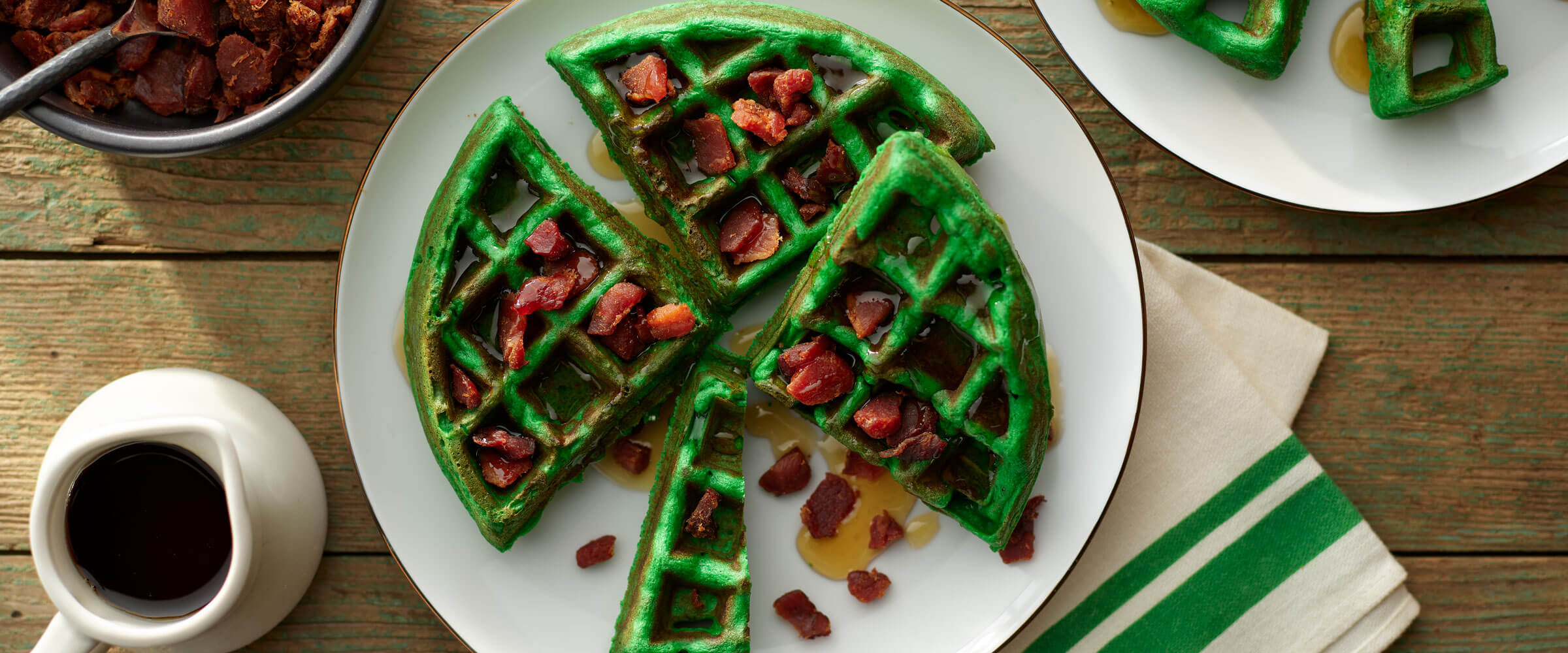 Green shamrock waffle and Bacon on white plate with extra syrup on side