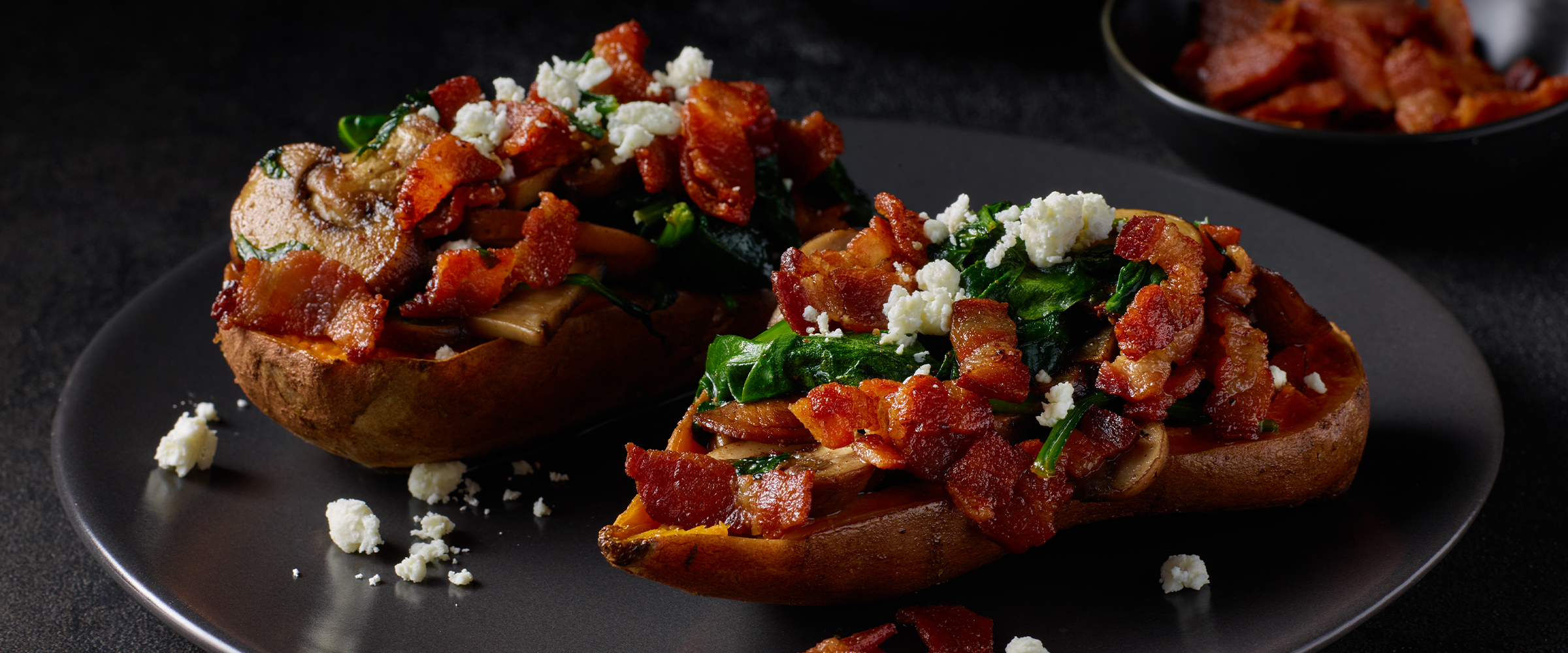 Two bacon and spinach sweet potatoes Florentine on a black plate.