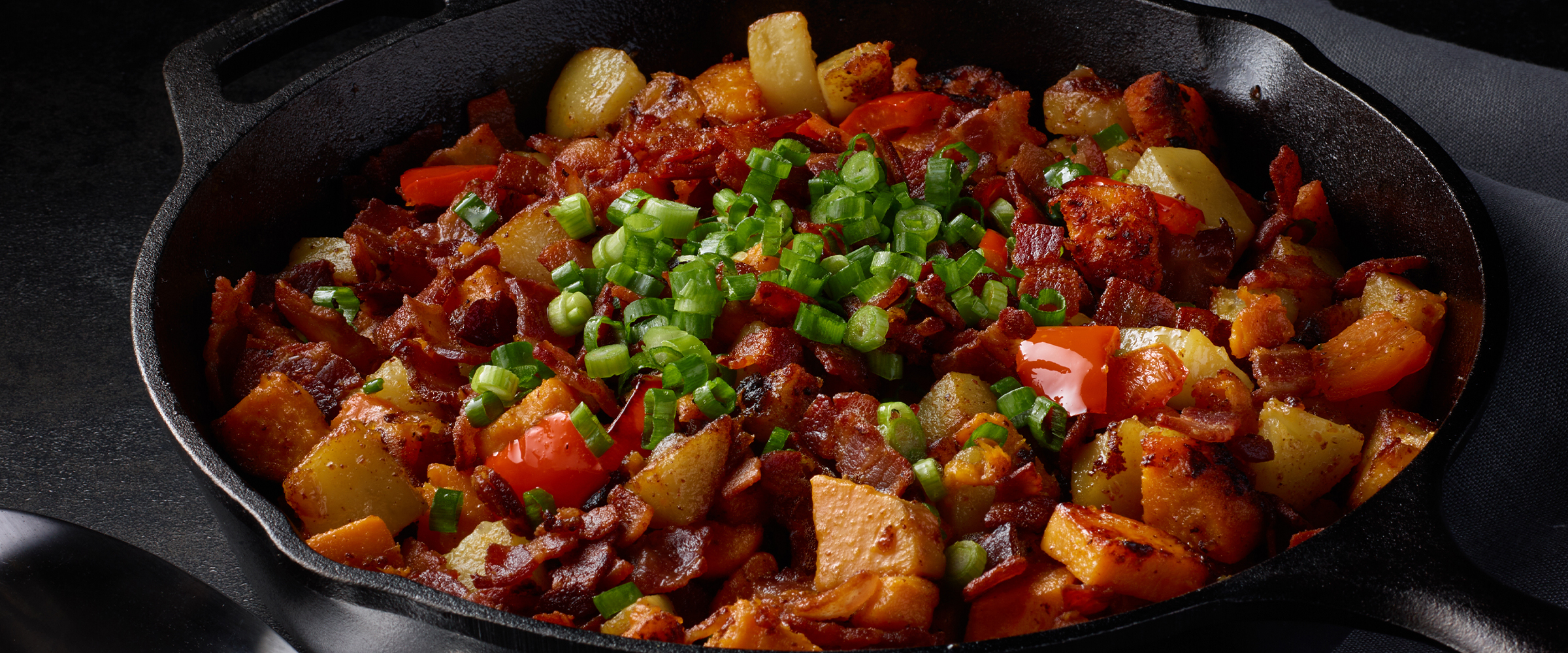 Sweet potato and bacon hash in a black cast iron skillet.