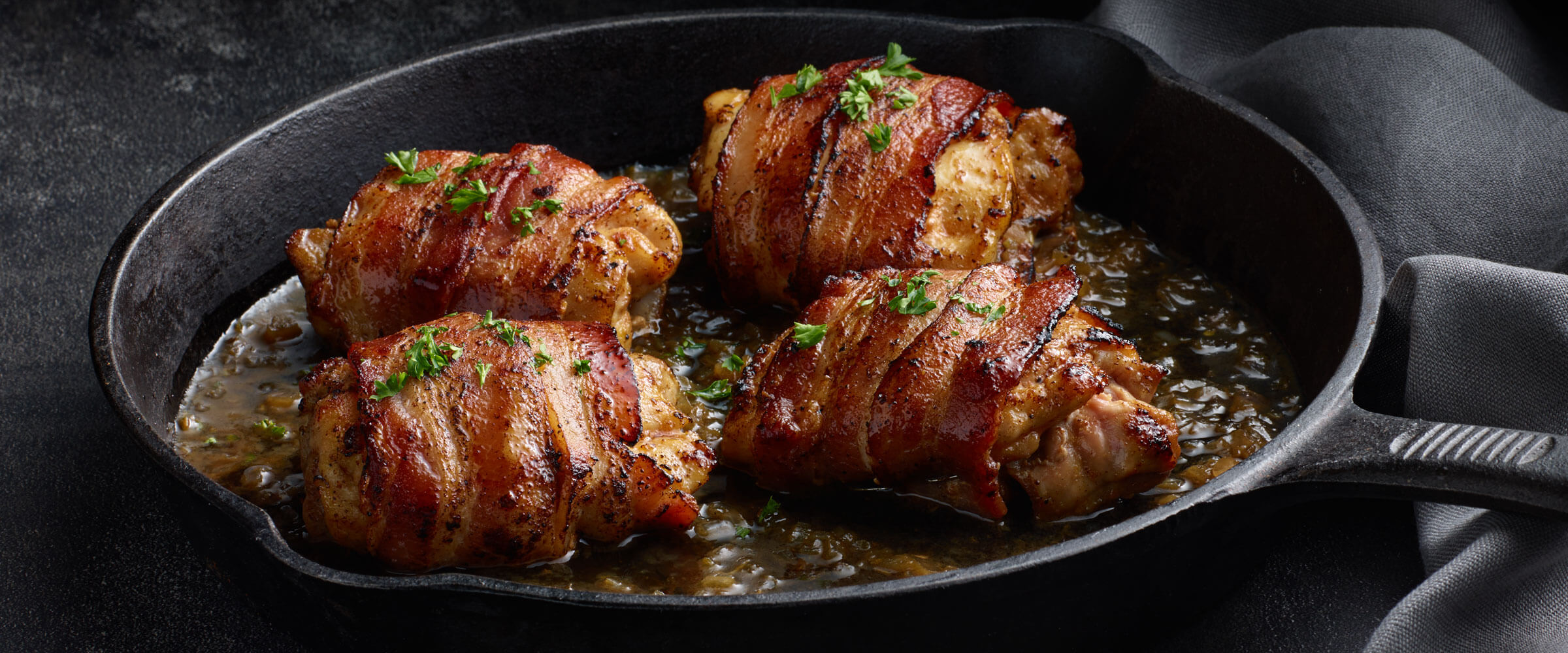 Apple Cider Bacon-Wrapped Chicken Thighs in cast iron skillet