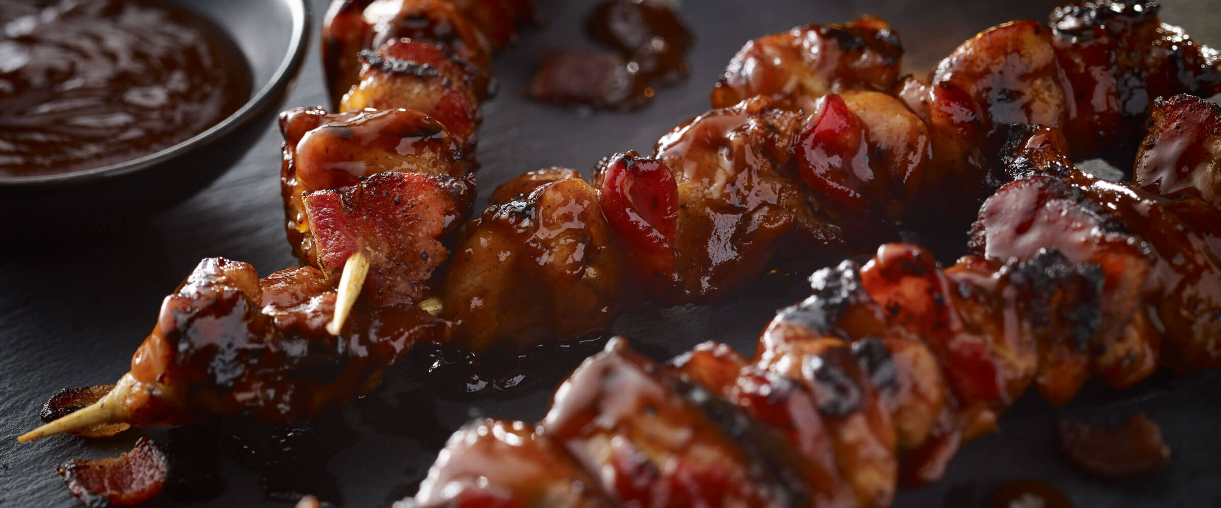 Bacon Bourbon Barbeque Chicken Kabob on black platter with dipping sauce