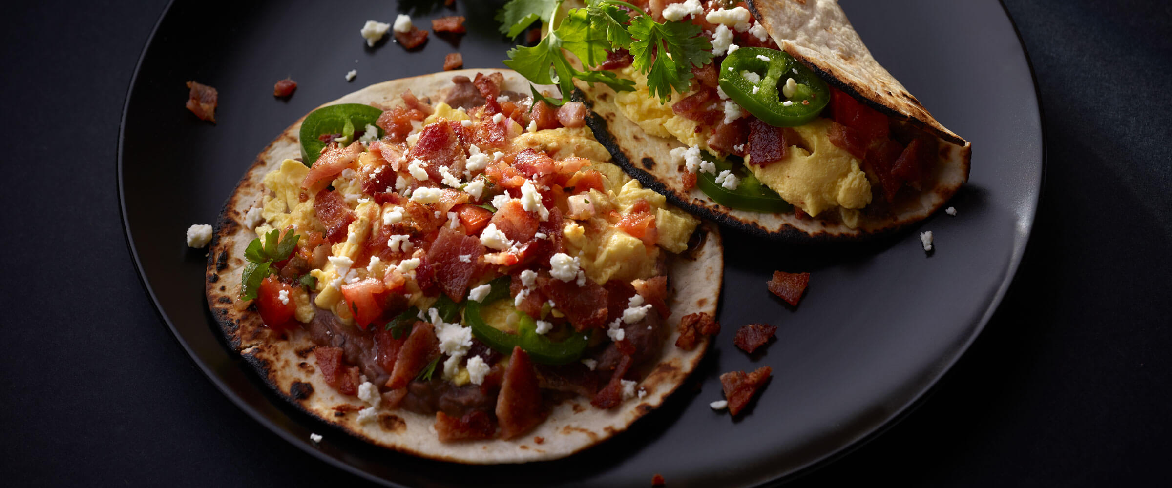 Bacon Breakfast Street Tacos garnished with cilantro on black plate