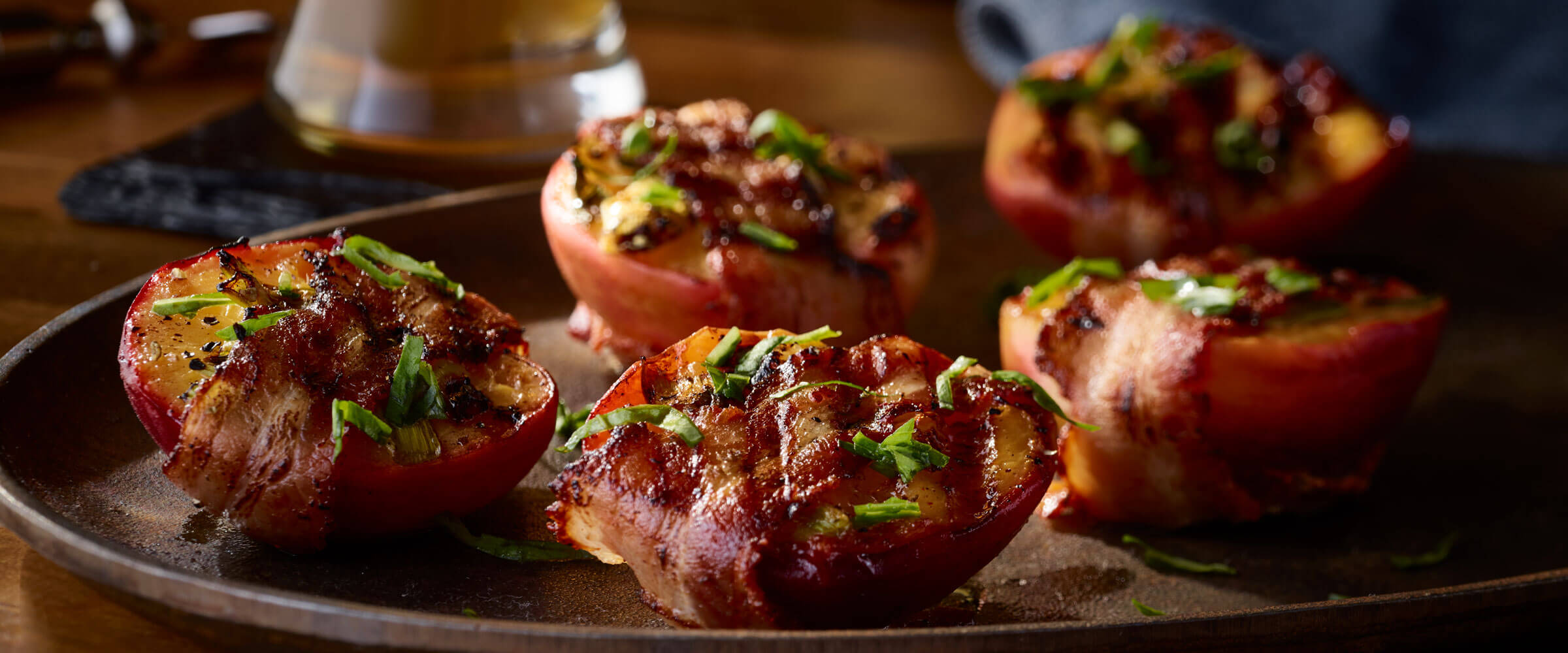 Bacon Wrapped Peaches topped with garnish on brown plate