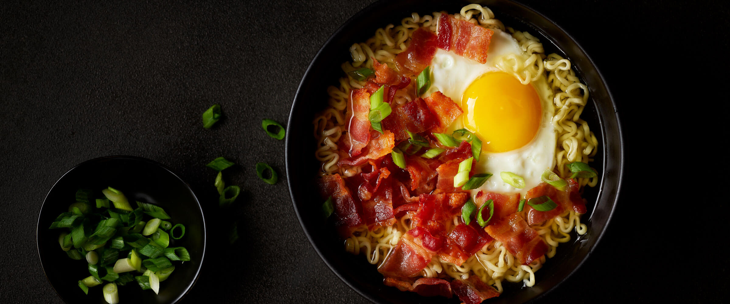 Bacon and Egg Ramen in black bowl topped with green onions