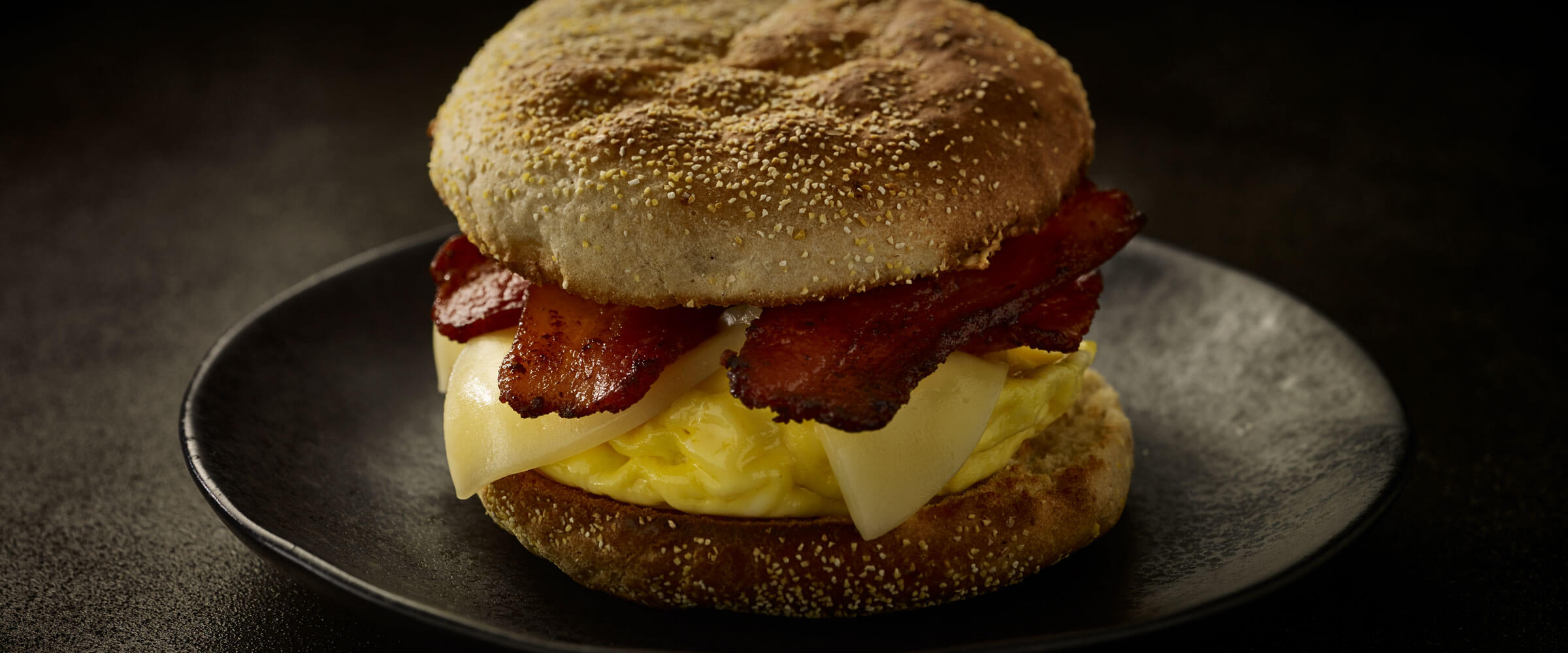 Bacon and English Muffin Sandwich with egg on black plate