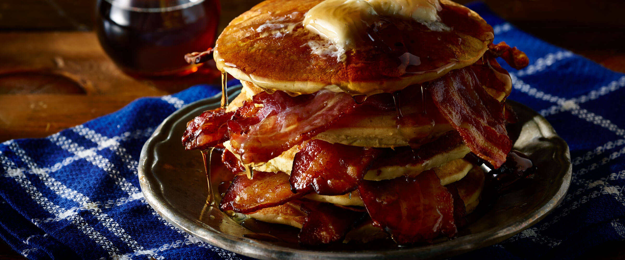 Bacon Pancakes piled high with syrup and butter on blue and white placemat
