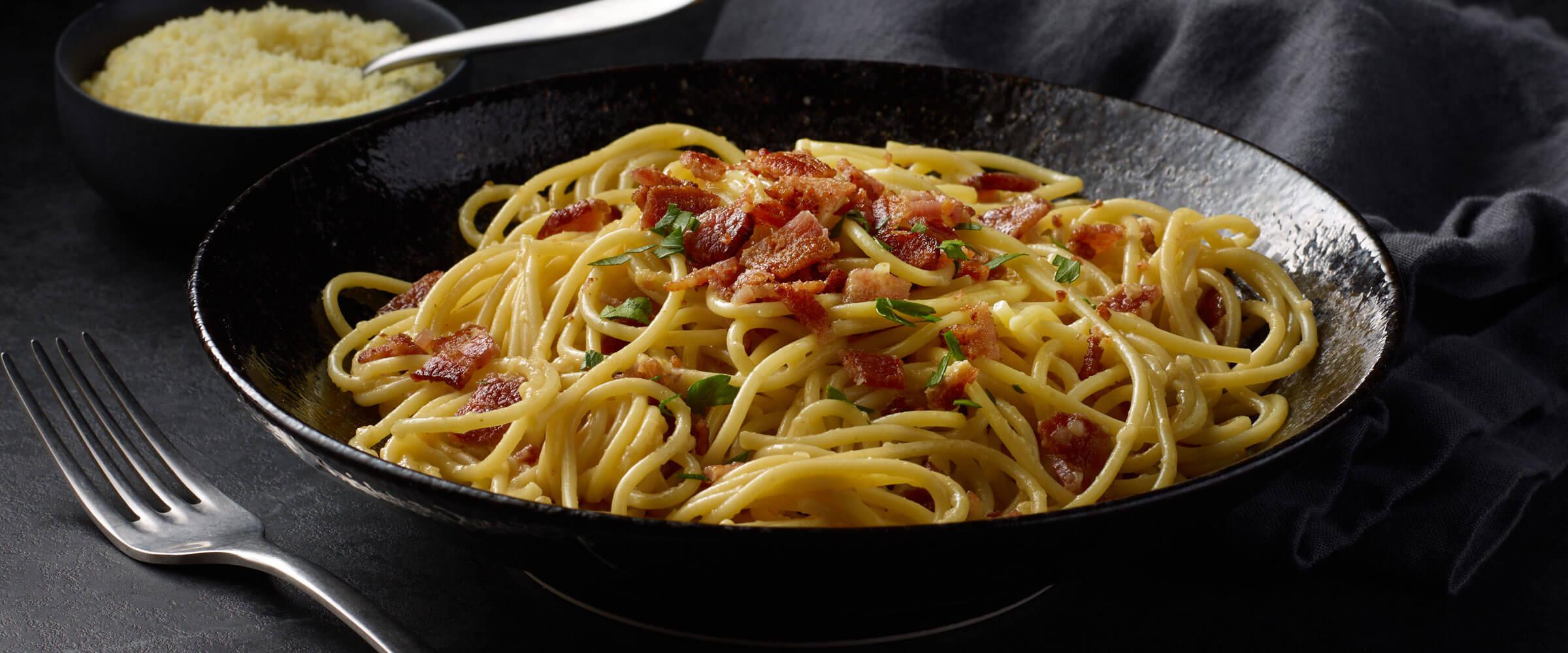 Pasta Carbonara topped with bacon in black bowl with fork