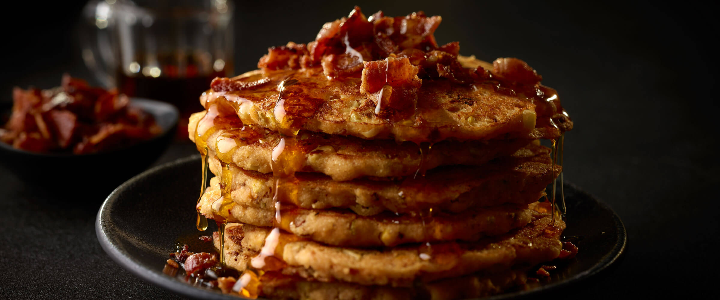 Bacon and Corn Griddle Cakes piled high topped with bacon and syrup