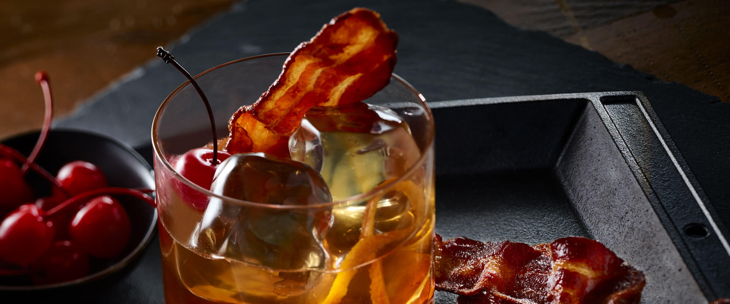 Cherrywood Bacon-Infused Manhattan in glass with cherry and bacon slide