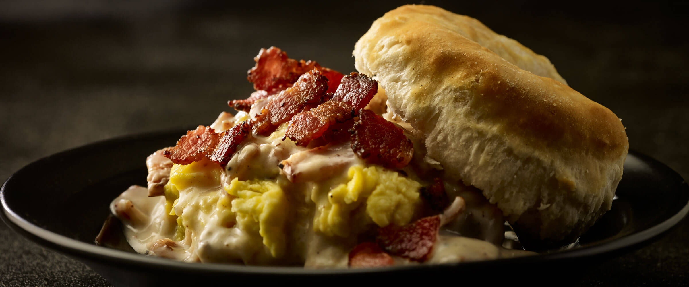 Biscuits and gravy topped with bacon on black plate