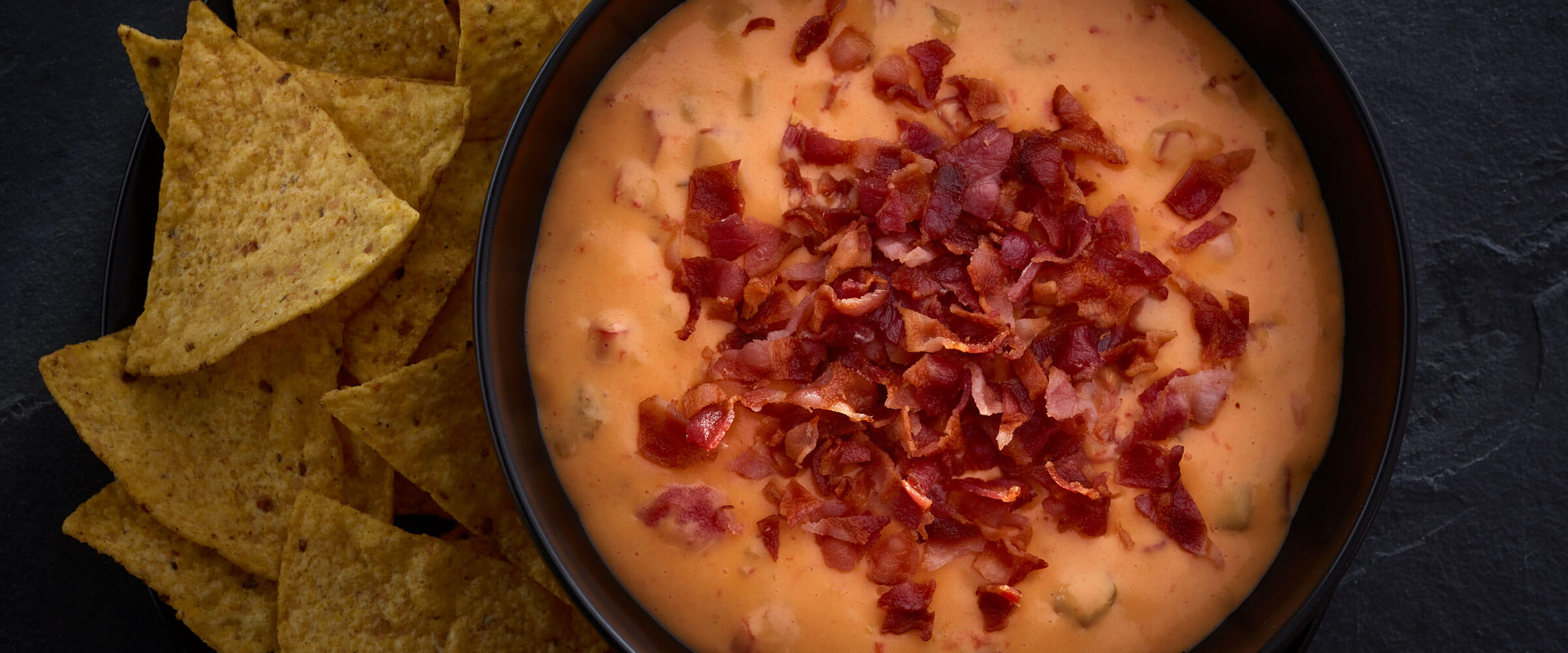 Bacon queso dip in bowl with chips on side