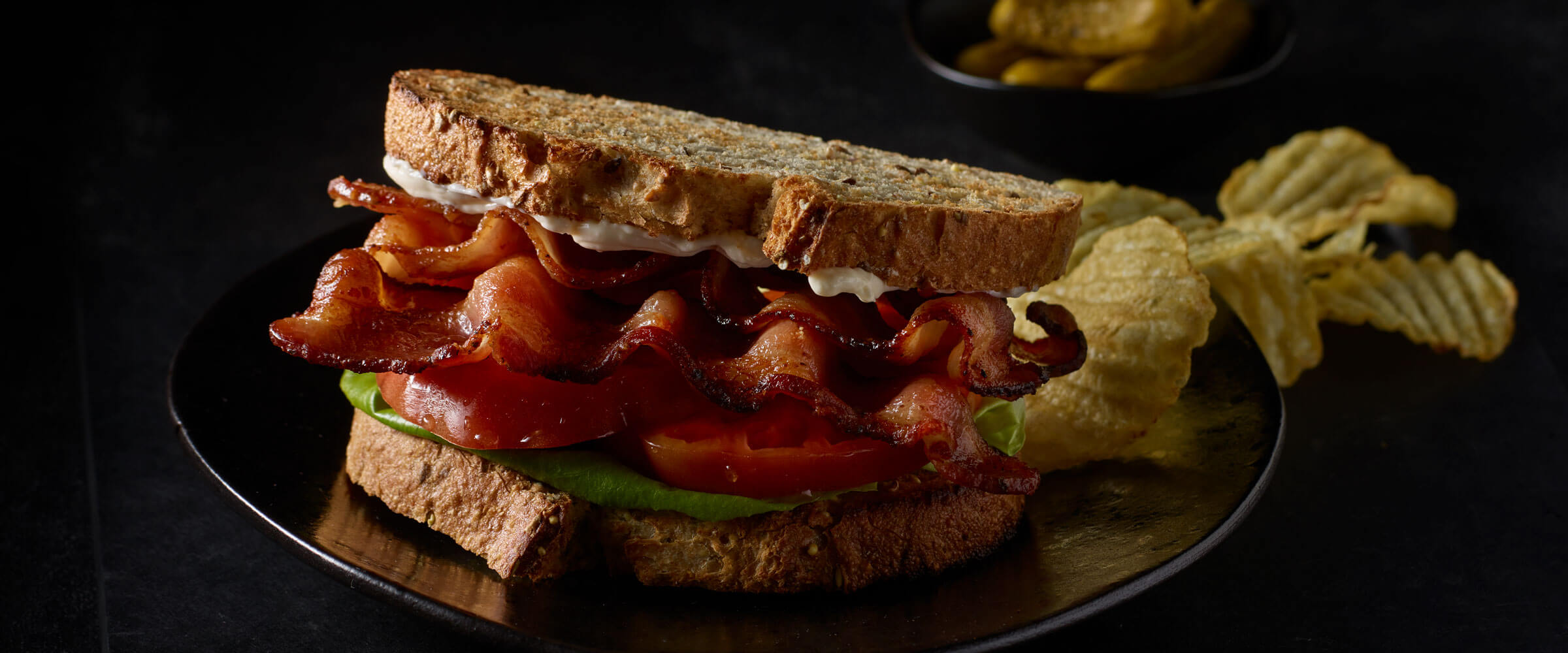 BLT on wheat bread with side of potato chips on black plate