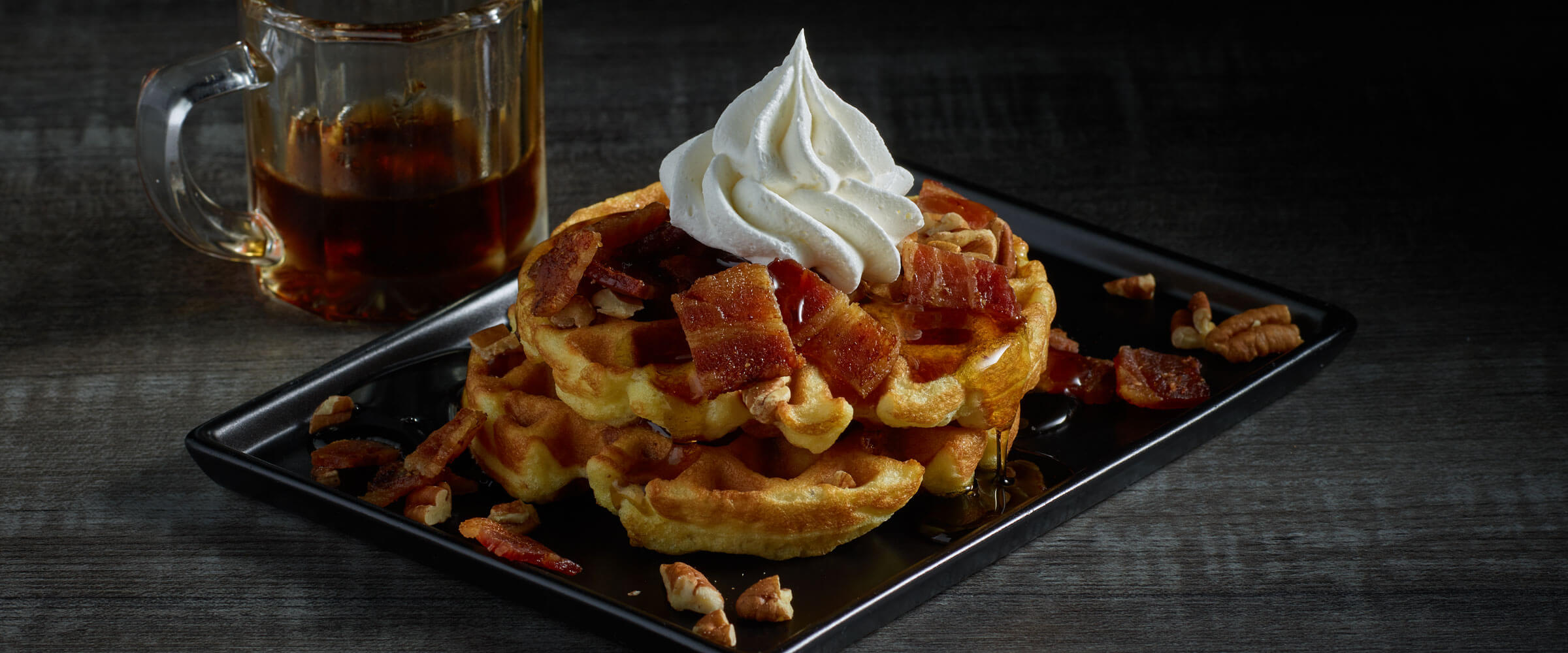 Sweet and Savory Bacon Cream Cheese Chaffles on black plate with extra syrup