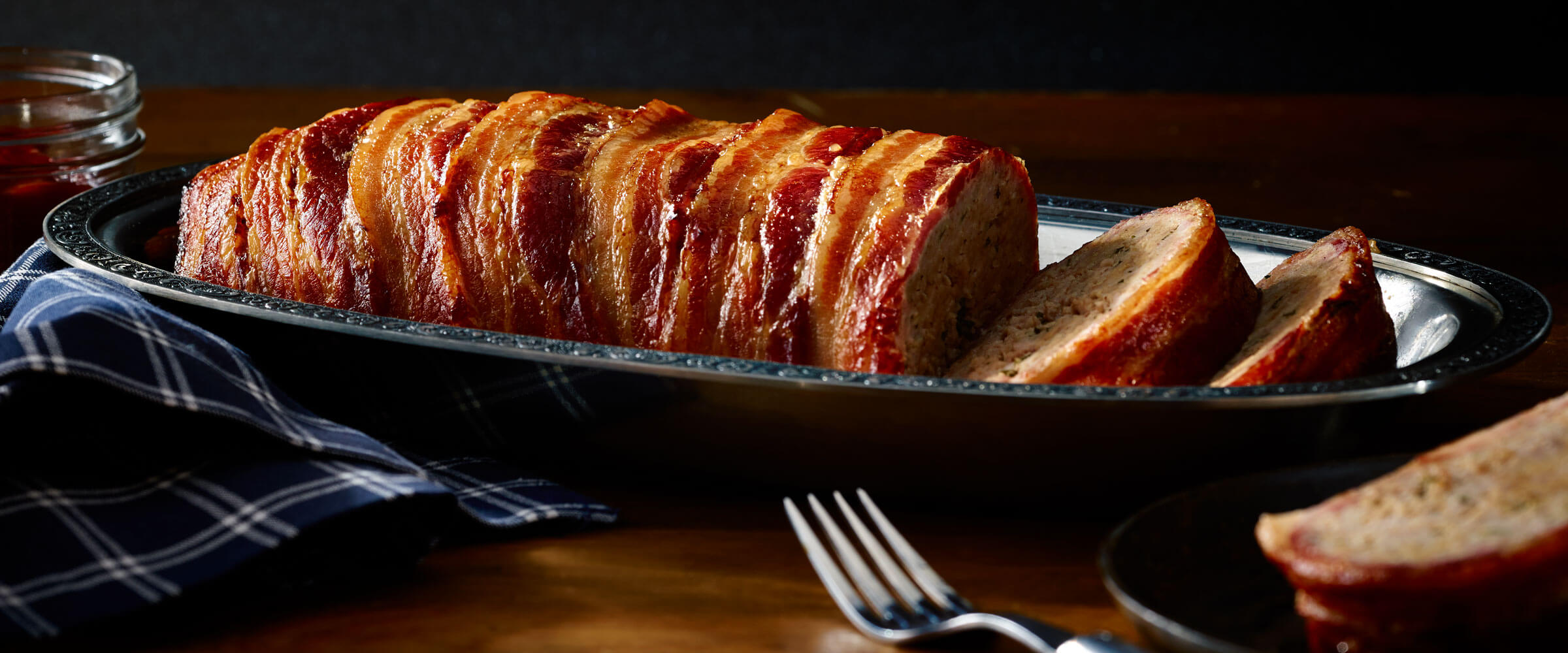 Bacon Wrapped Meatloaf in serving dish with blue napkin