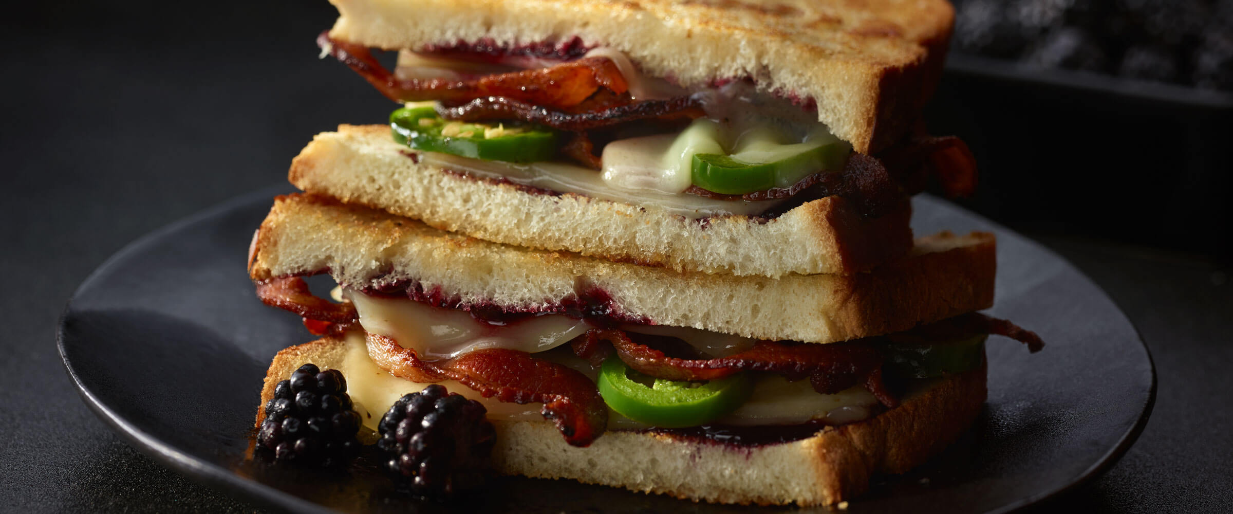 Blackberry Bacon Grilled Cheese with jalapenos on black plate