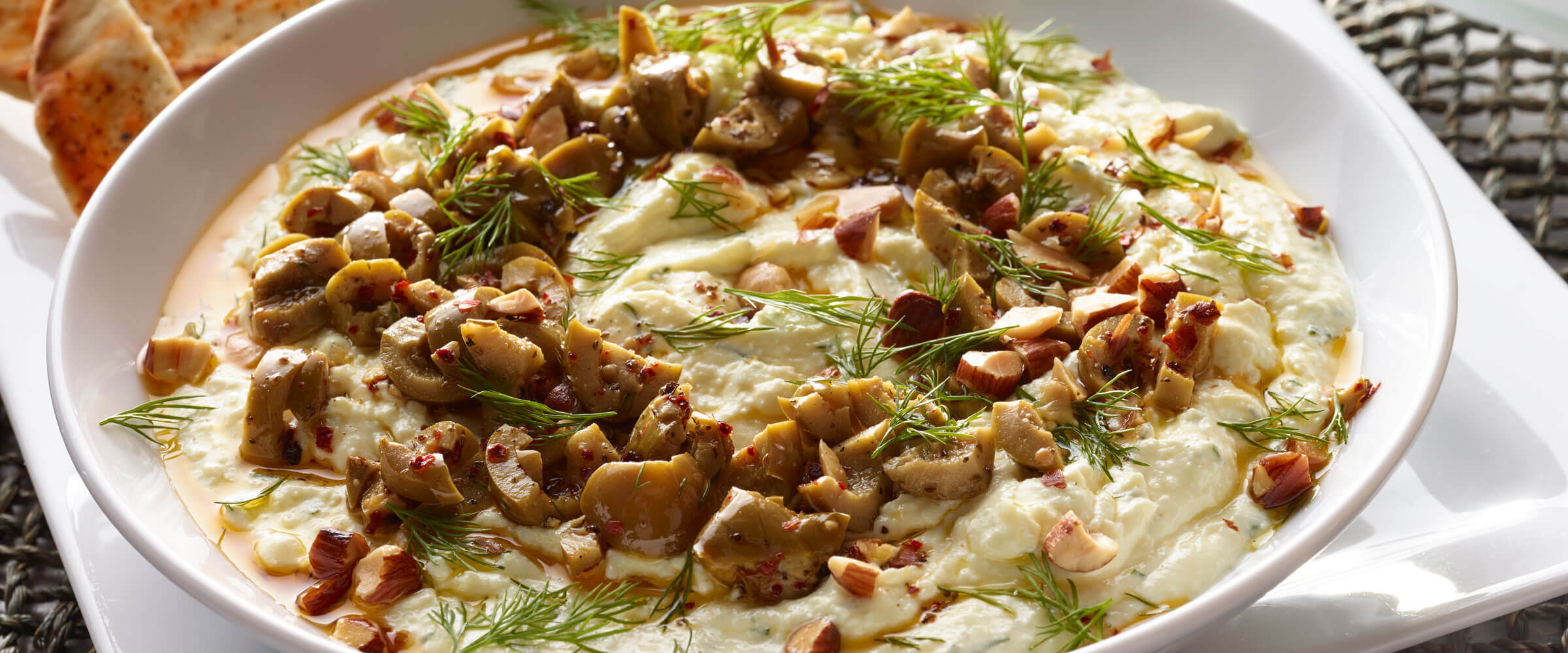 Garlic-Bacon Feta Dip topped with olives and garnish in white bowl