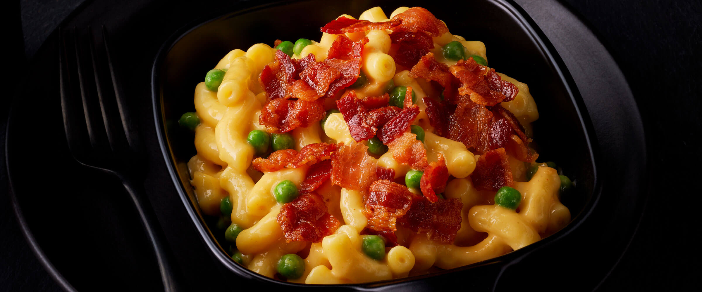 Bacon, Macaroni and Cheese, and Peas in black dish with fork