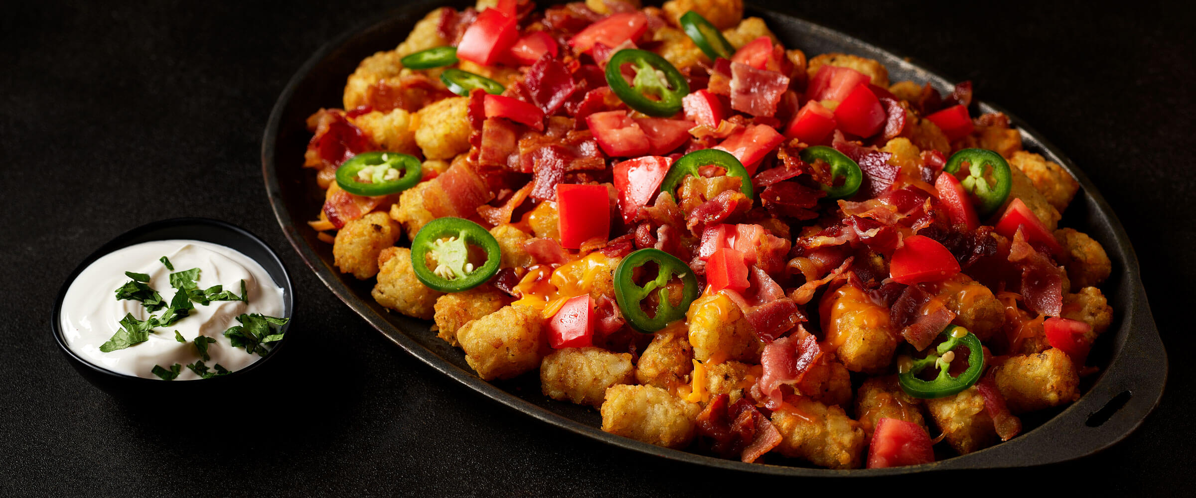 Loaded Tatchos topped with jalapenos and tomatoes with sour cream on side