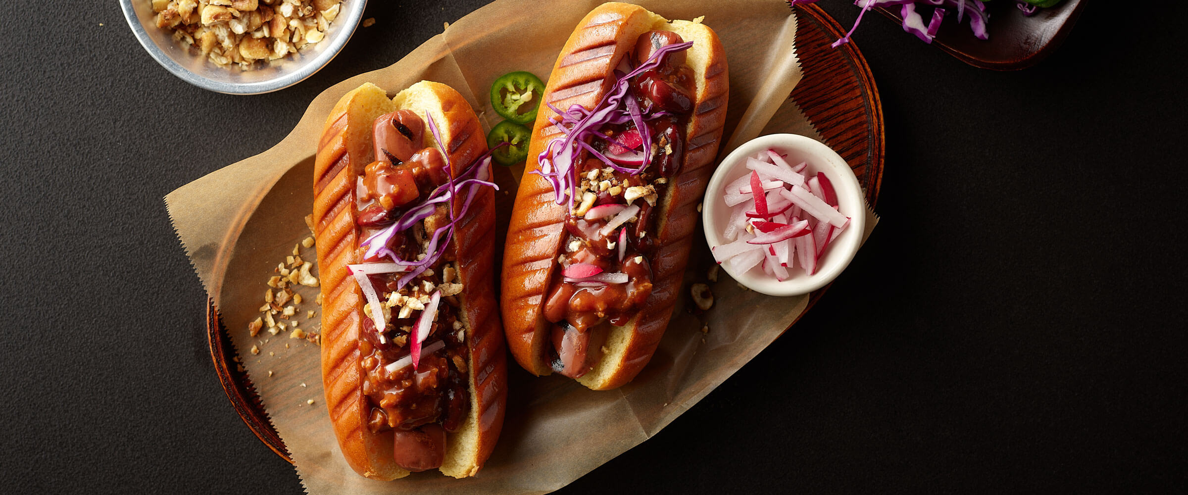 Plant-Based Chili Dogs with onion and slaw topping on wooden platter