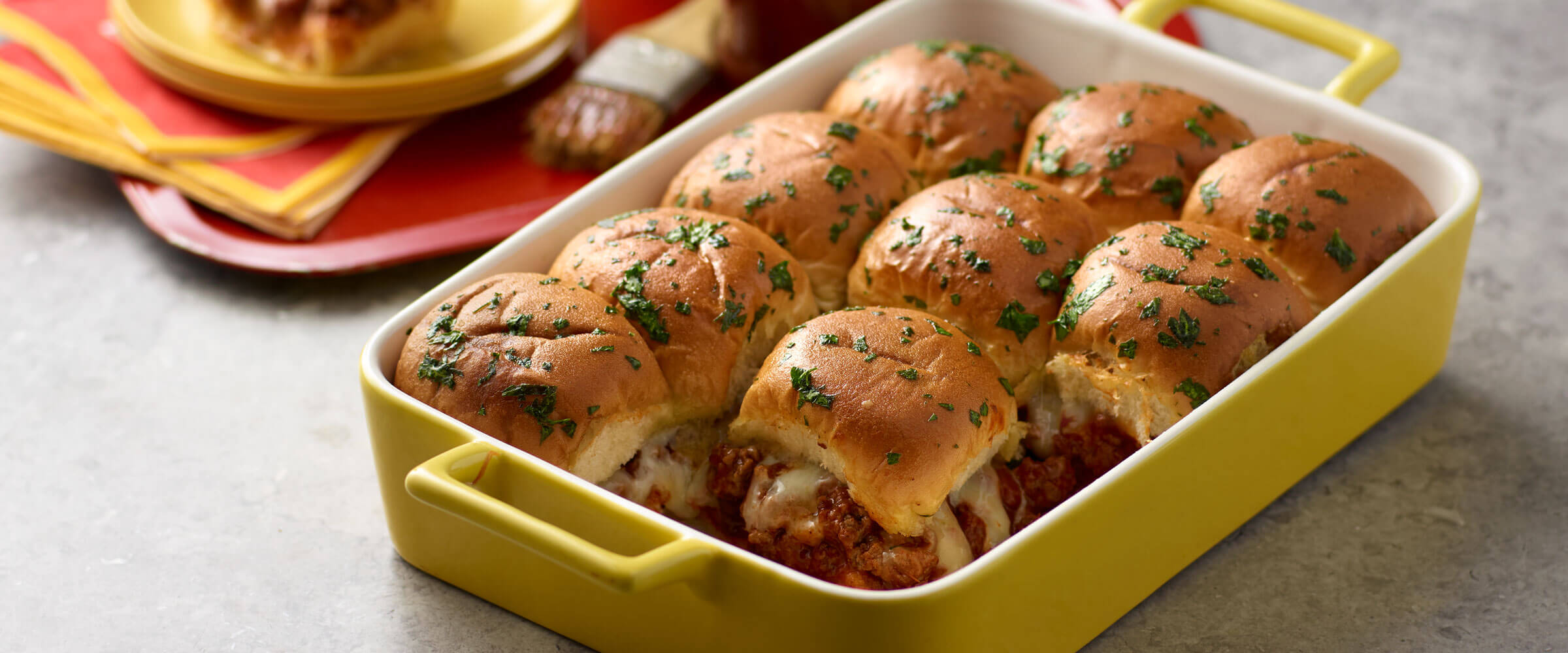 Baked BBQ Chili Cheeseburger Sliders in yellow dish topped with garnish