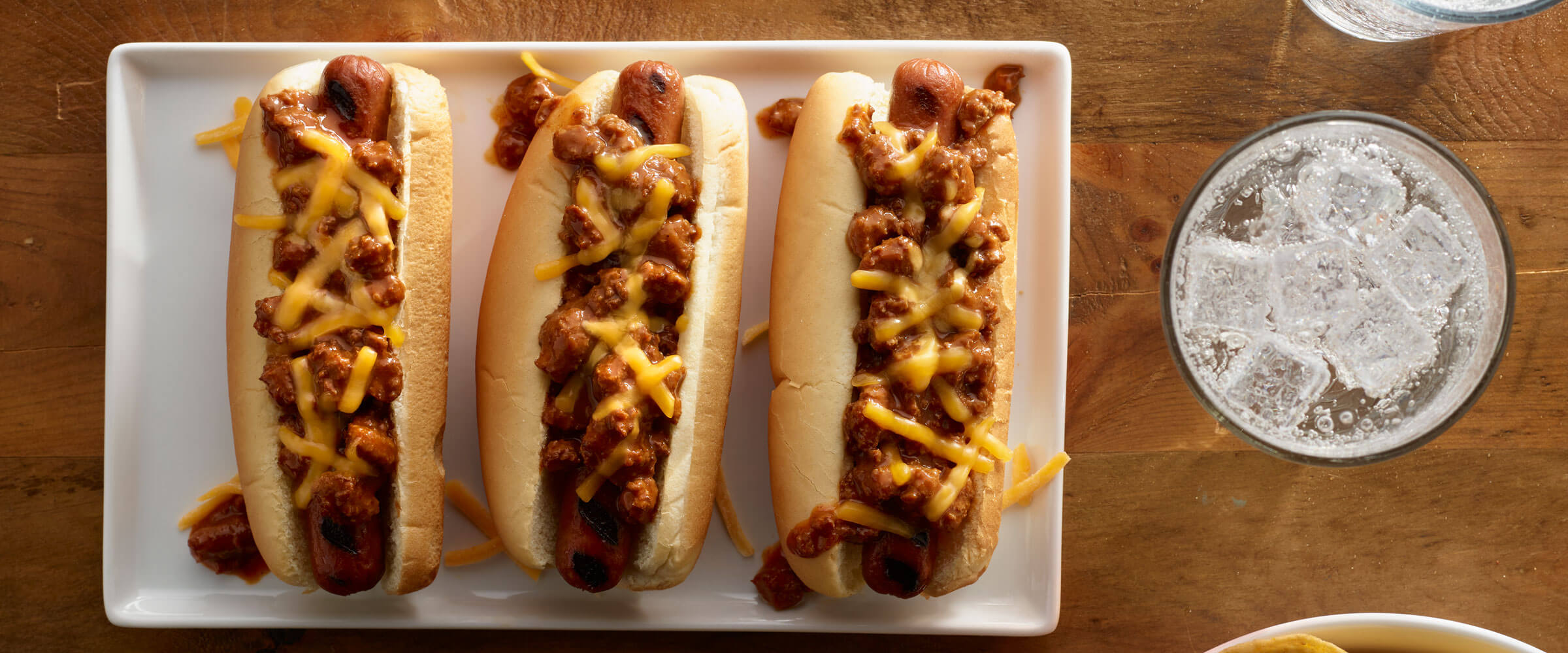 Chili Dogs topped with Cheese on white platter with drink on the side