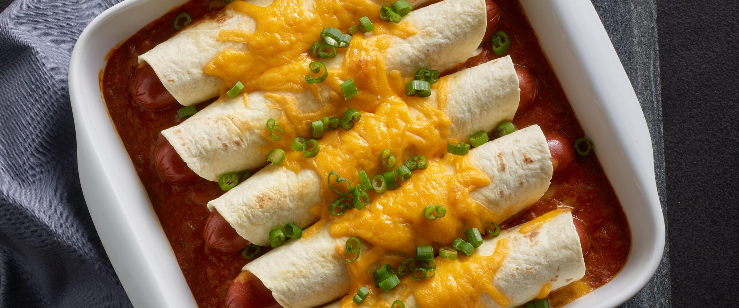Cheesy Coney Island Chili Dog Bake in white dish topped with cheese and green onions