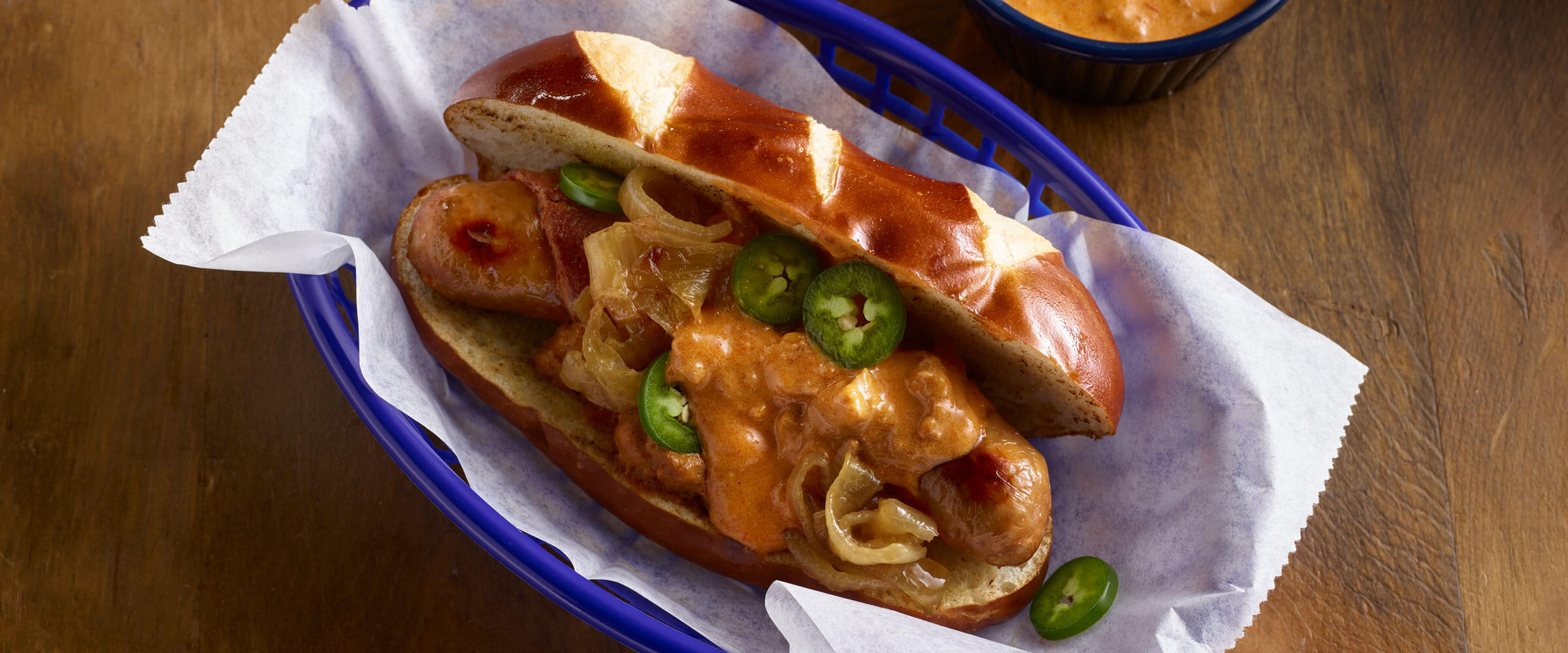Chili Beer Cheese Bacon Brat topped with jalapenos on white paper in blue basket