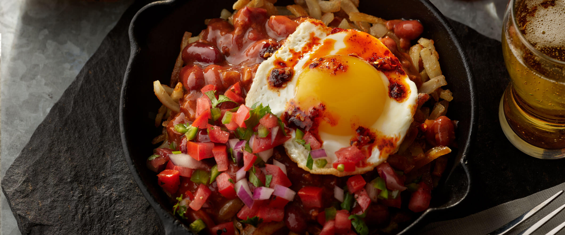 Chili Breakfast Bowl topped with egg, salsa and hot sauce in cast iron skillet