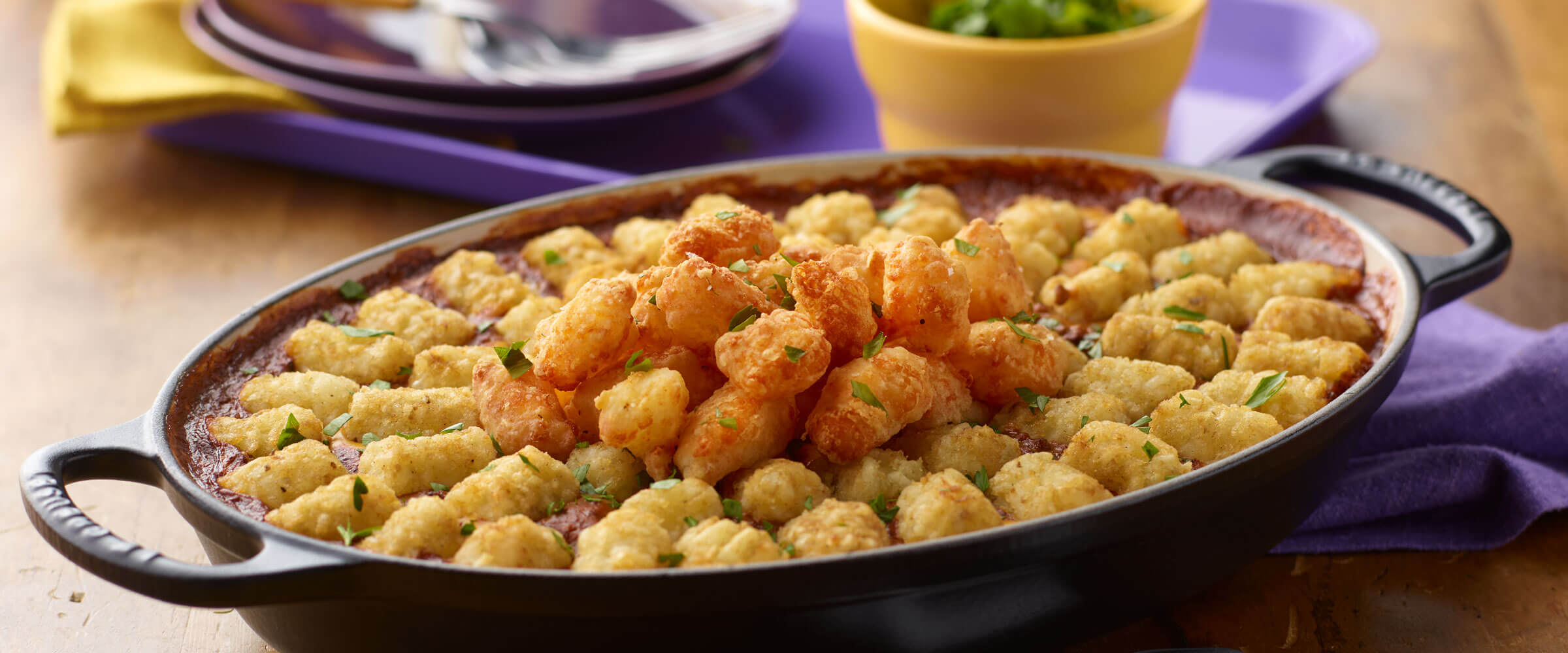 Chili Cheese Dip Hot Dish topped with tator tots in black dish with blue napkin