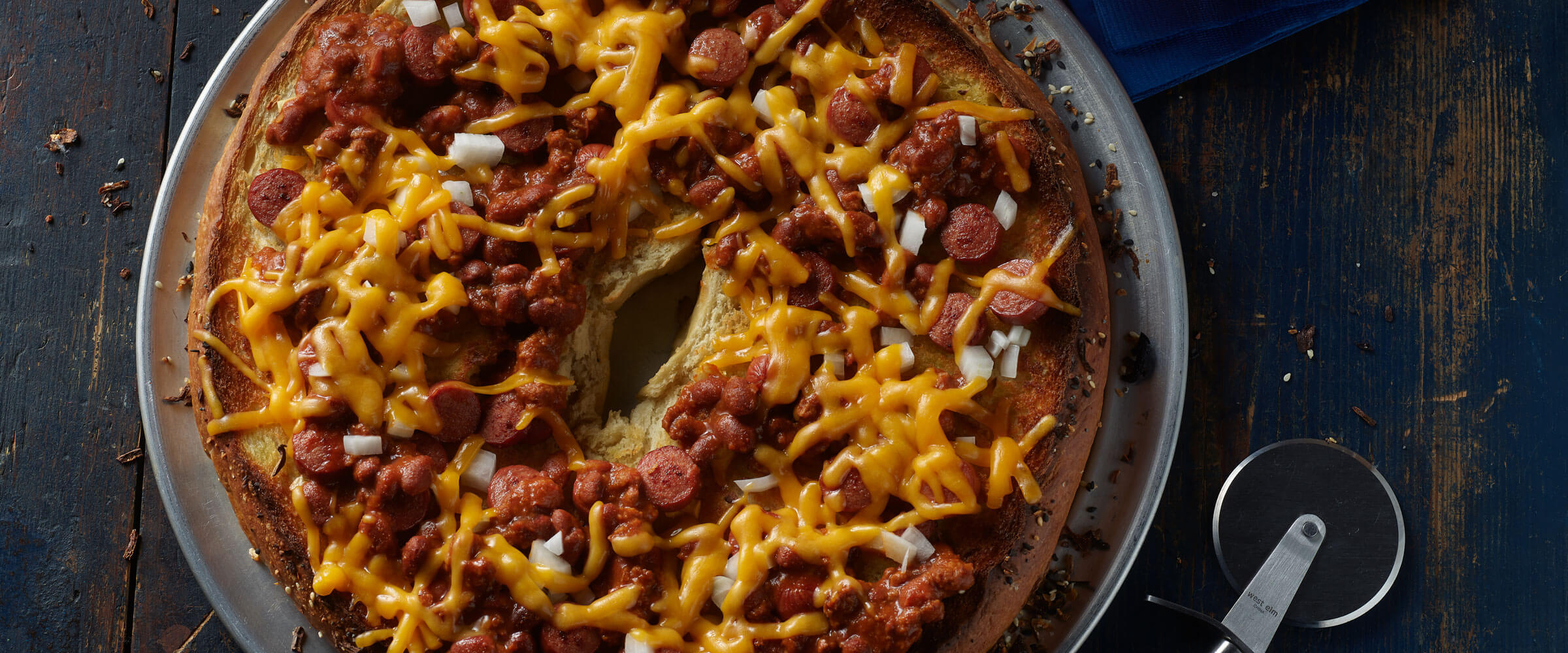 Chili Cheese Dog Bagel Pizza on pizza pan with pizza cutter