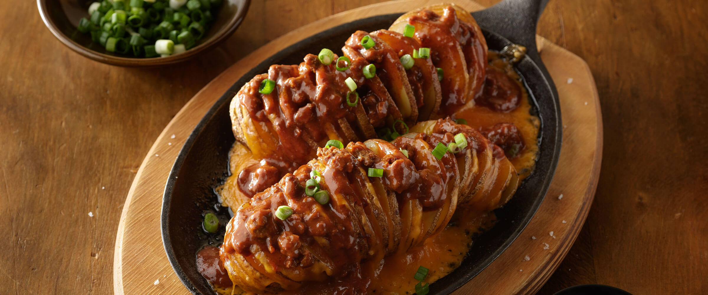 Chili Cheese Hasselback Potatoes in cast iron skilled topped with green onions