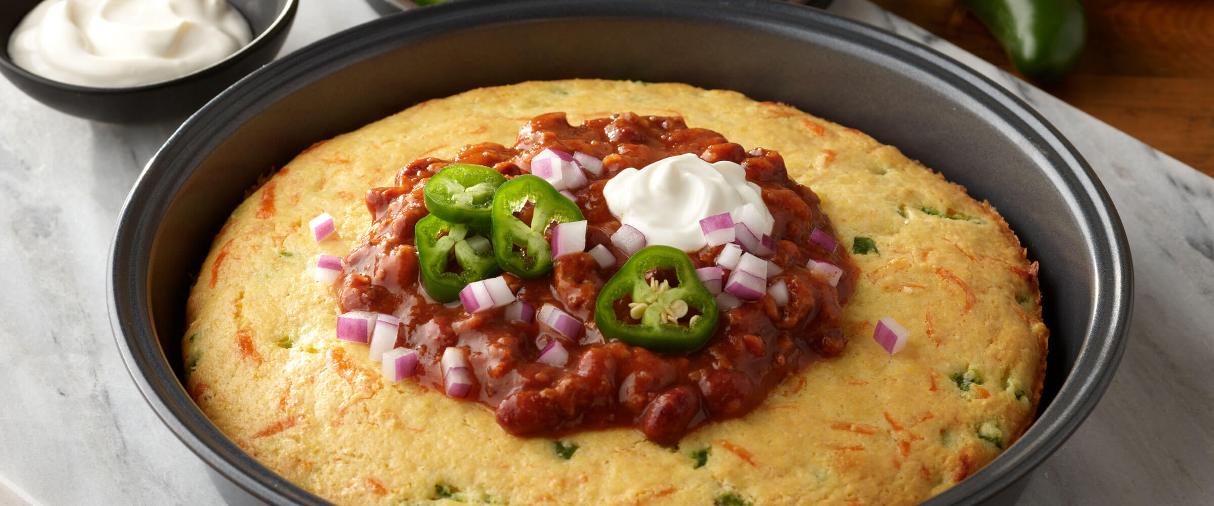 Chili Cornbread Bowl topped with jalapenos, red onions and sour cream in metal pan